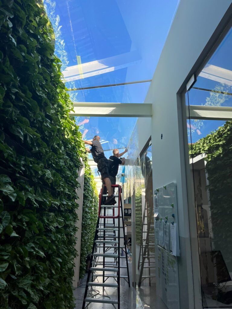 Dorigo Rosbag op de ladders om zonwerende raamfolie te plaatsen